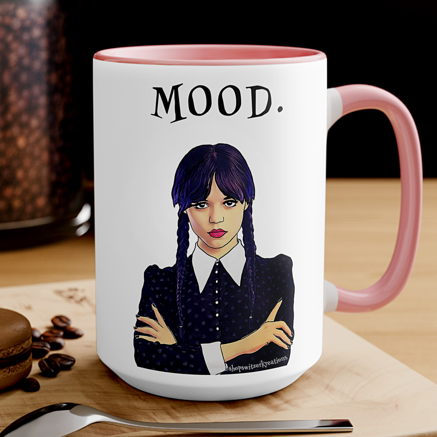 A pink and white ceramic coffee mug featuring an illustration of Wednesday Addams with a deadpan expression. Below the image is the word “MOOD” in bold, black text. The design is printed on both sides, making it suitable for right- or left-handed users. A perfect gift for fans of dark humor and gothic style.