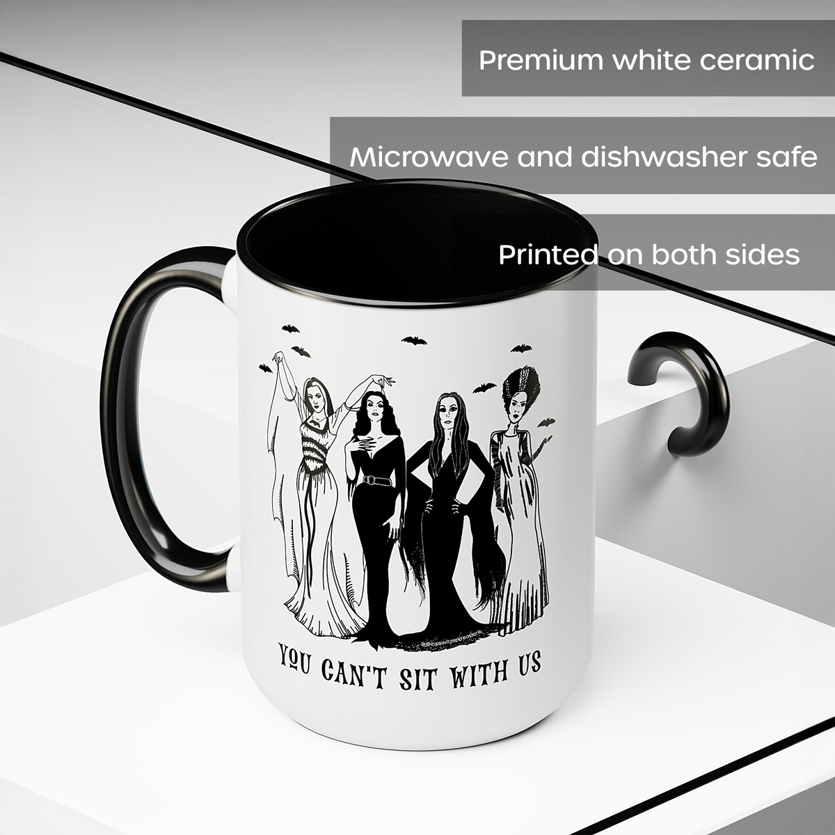 A white ceramic mug with a black interior, black handle, and black printed graphic of four women with the text 'YOU CAN'T SIT WITH US.' The image includes text overlays stating 'Premium white ceramic,' 'Microwave and dishwasher safe,' and 'Printed on both sides.