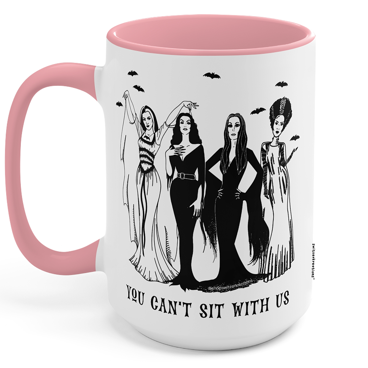 A white ceramic mug with a pink handle and interior, featuring a black line art illustration of four gothic women and the text 'YOU CAN'T SIT WITH US' printed on the front.